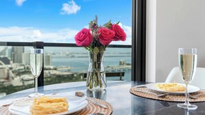 Une table avec un vase de roses roses, deux assiettes de pâtes et deux verres de vin, avec une vue sur la ville à travers une fenêtre.