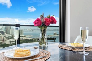 Een tafel met een vaas roze rozen, twee borden pasta en twee glazen wijn, met uitzicht op een stadsgezicht door een raam.