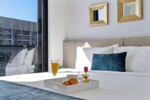 Ein Hotelzimmer mit einem Bett, einem Frühstückswagen mit Croissants, einem Glas Orangensaft und einer Blume.