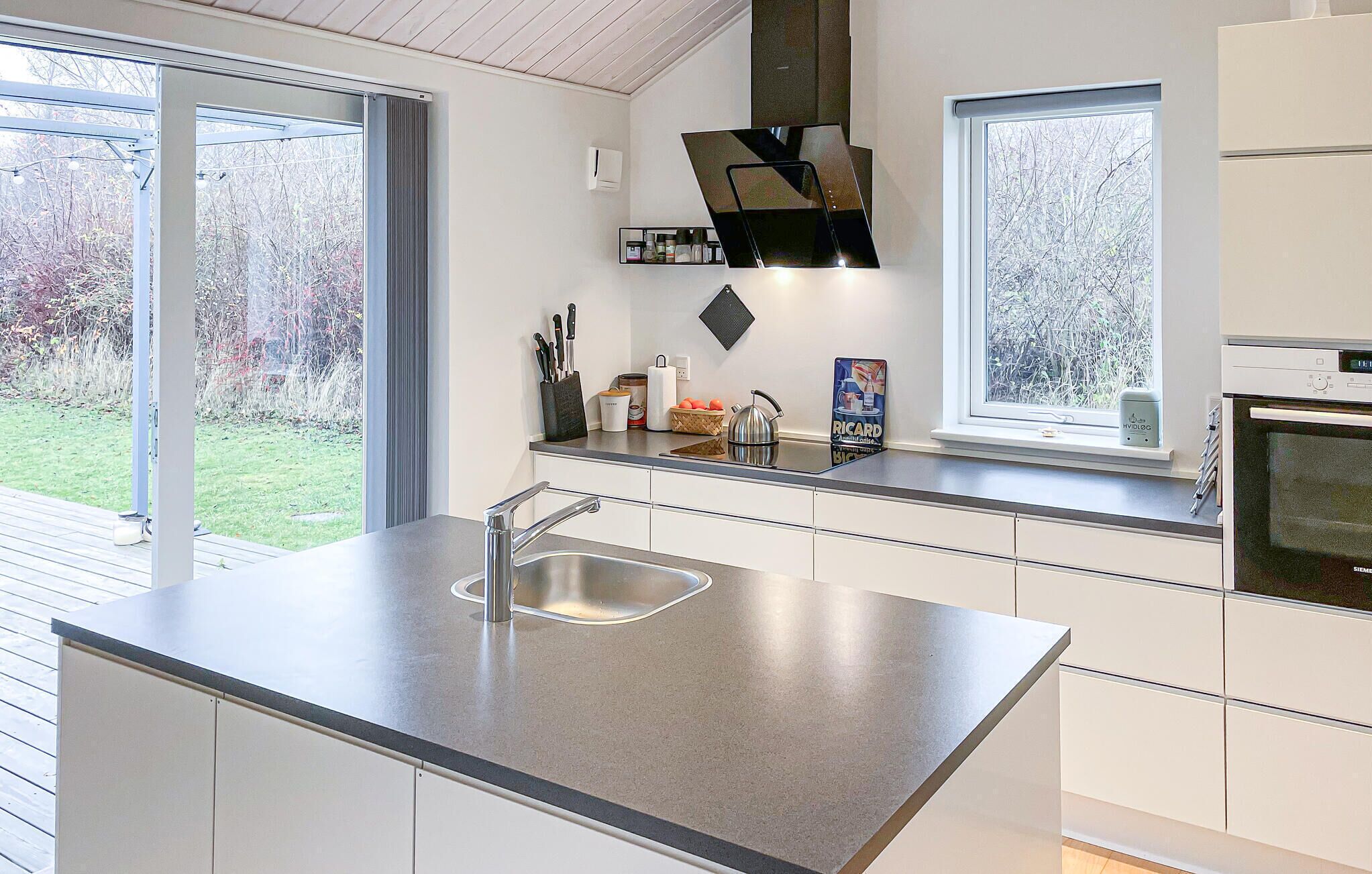 A modern kitchen with a large island, stainless steel appliances, and large windows offering views of the outdoors.
