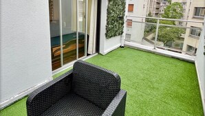 A balcony with artificial green turf, a wicker sofa, and a sliding glass door. - Family Friendly 2BR Apartment • Terrace - Parking - Neuilly-sur-Seine/La Defense (Neuilly-sur-Seine)