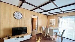 A modern living room with a wooden ceiling, a flat-screen TV, a dining area with a table and chairs, and a large window providing natural light. - Family Friendly 2BR Apartment • Terrace - Parking - Neuilly-sur-Seine/La Defense (Neuilly-sur-Seine)