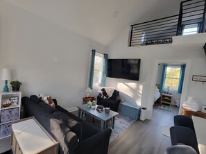 A modern living room with a sofa, a coffee table, and a TV. There is a staircase leading to an upper level. - Wild Horses - 4x4 Beach - Quiet & Cozy (Corolla)