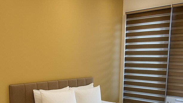 A neatly made bed with white linens and two rolled towels, a wooden nightstand with drawers, and a window with horizontal blinds. - The Miles Arms Hotel (Bristol)
