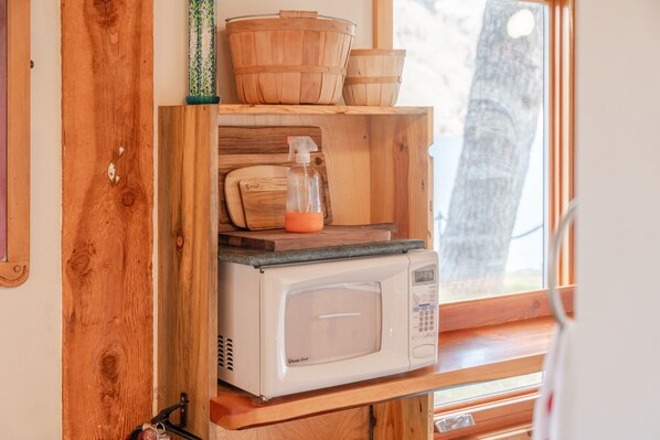 A white microwave rests on a built-in wooden shelf next to a bright window.