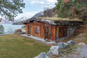 Exterior of a wood cabin with a sod roof overlooking a lake and distant mountains.