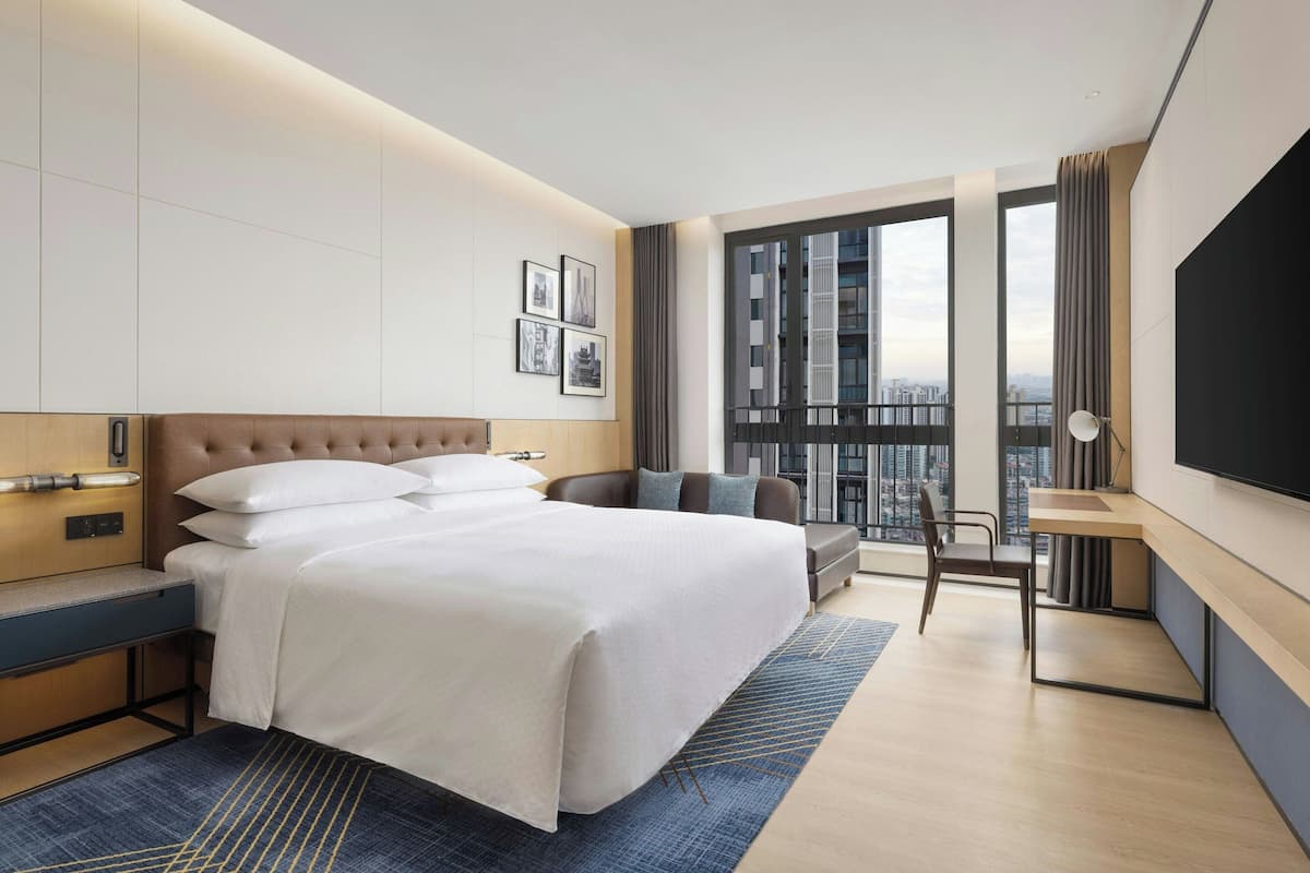 Una habitación de hotel moderna con una cama grande, un escritorio, una silla y un ventanal con vistas a la ciudad.