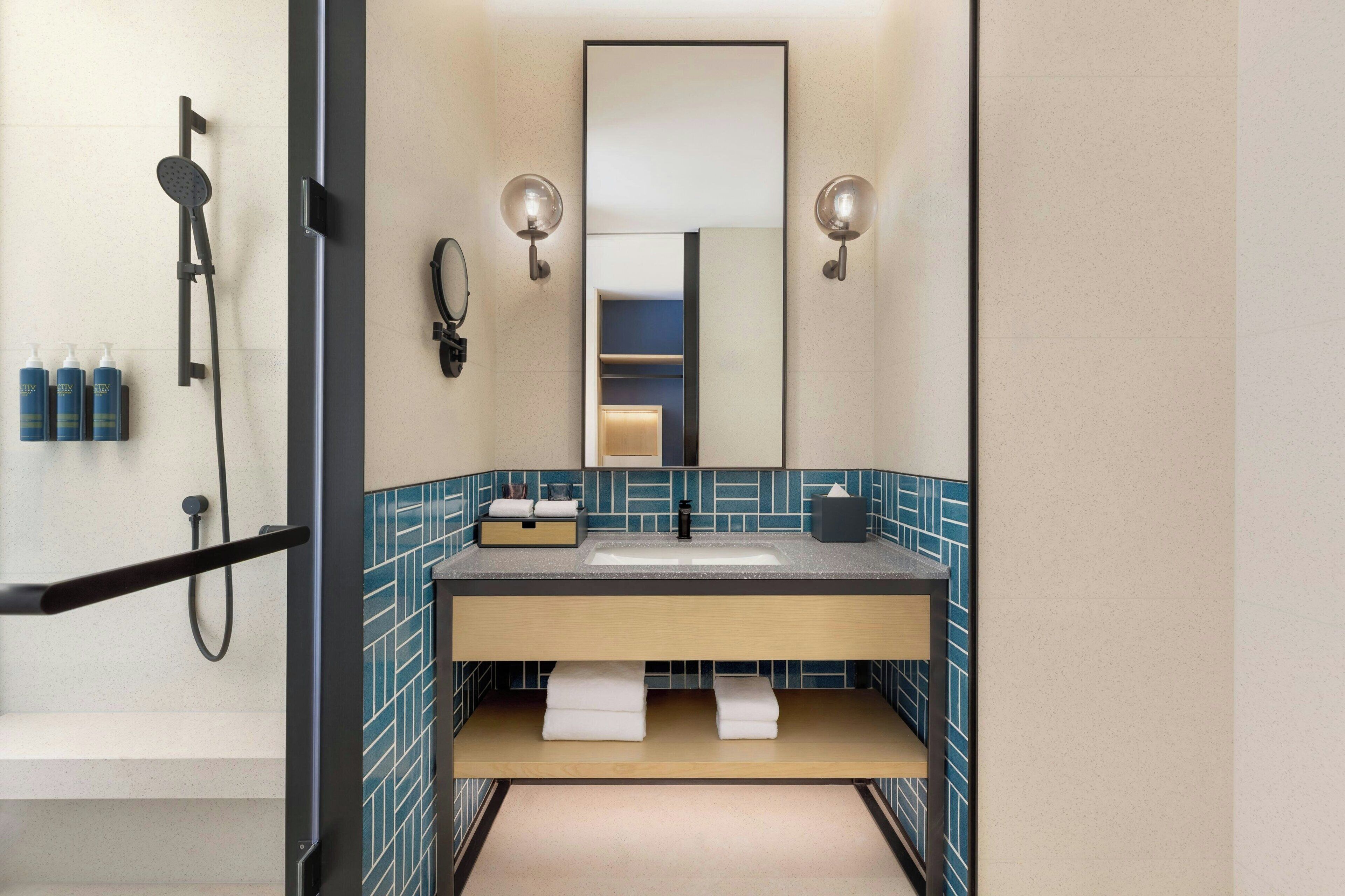 A modern bathroom with a sink, mirror, towel rack, and shower.