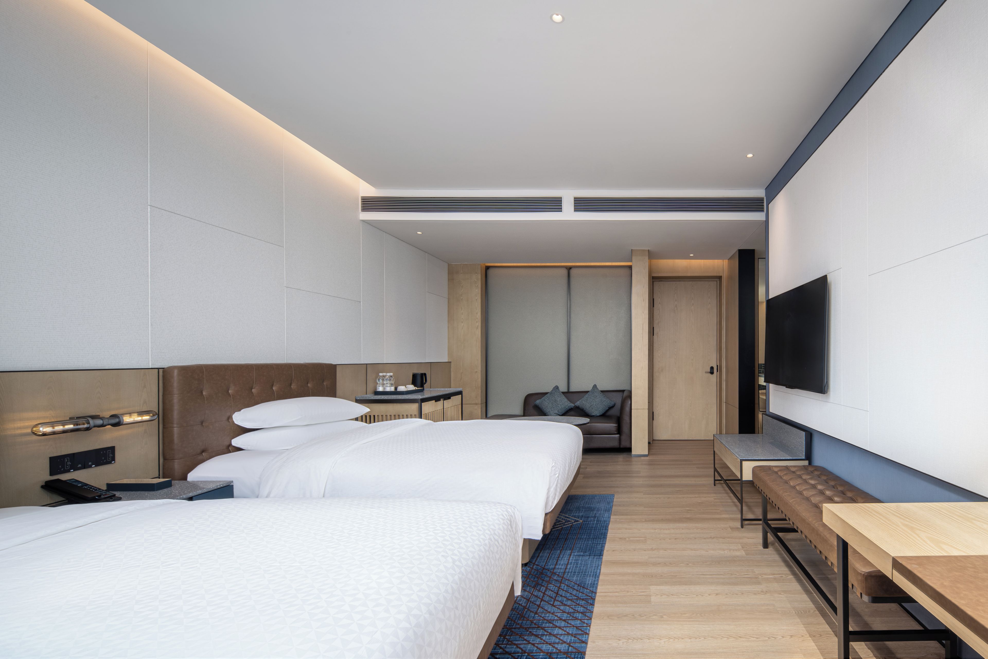 Una habitación de hotel moderna con dos camas, un escritorio, un televisor y una zona de estar.