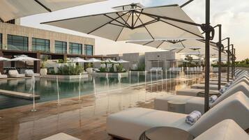 A poolside area with lounge chairs, umbrellas, and a modern building in the background.