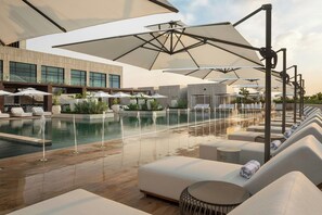 Un espace aménagé au bord de la piscine, avec des chaises longues, des parasols et un bâtiment moderne en arrière-plan.