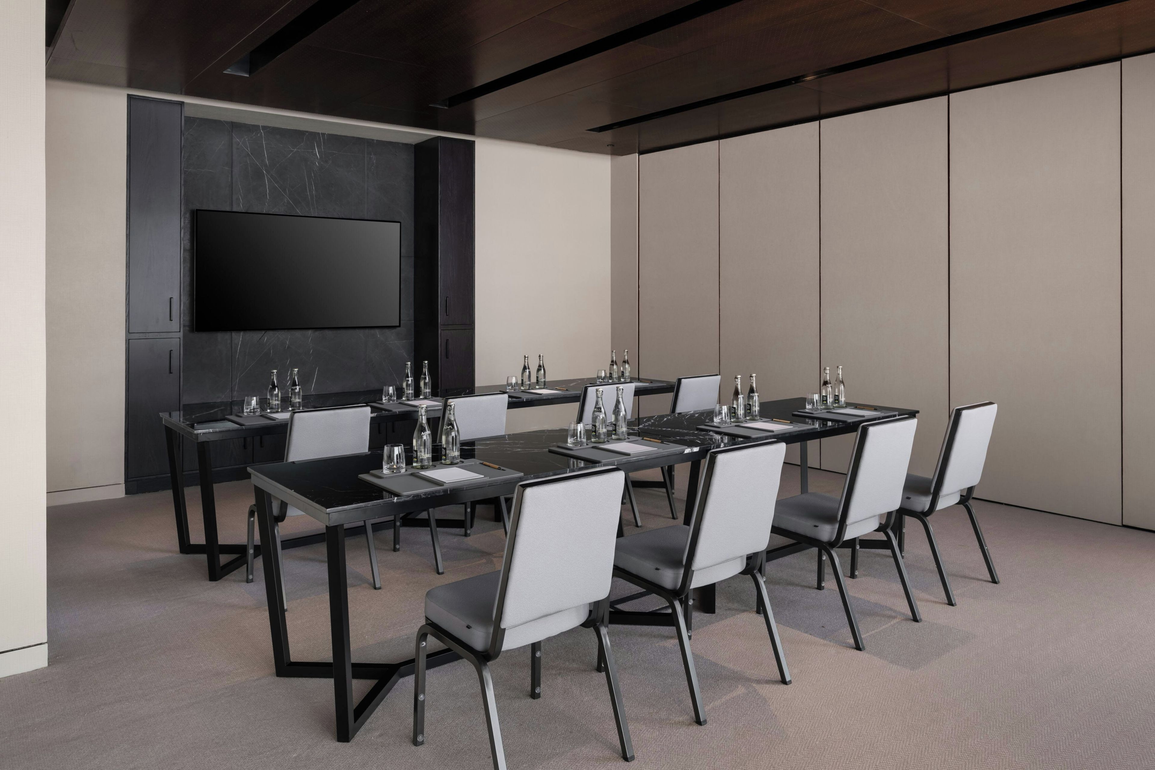 Una sala de conferencias moderna con una mesa larga, sillas y un televisor de pantalla plana montado en la pared.