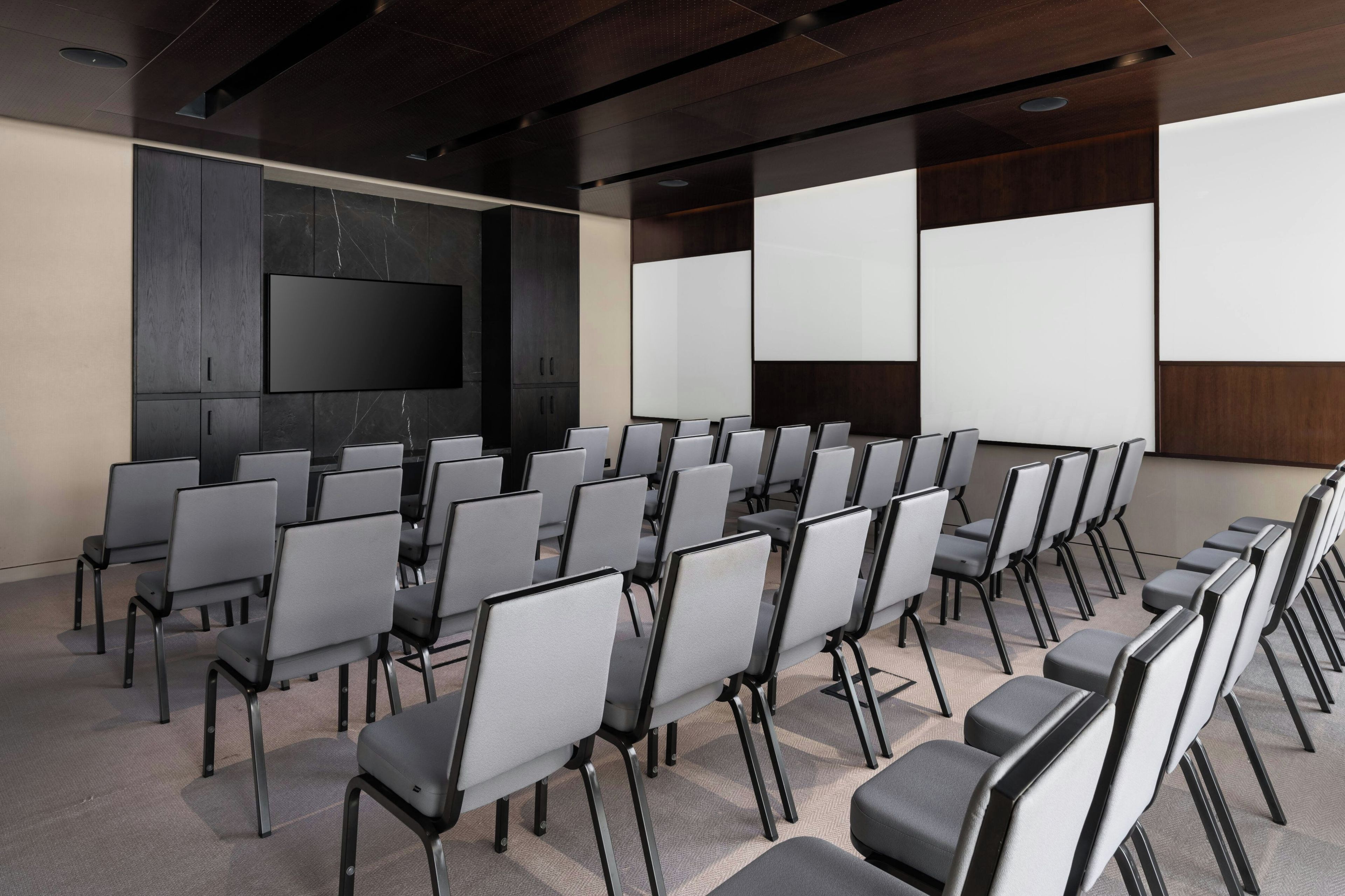 A conference room with rows of chairs, a large screen, and a wooden panel wall.
