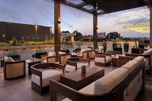 An outdoor seating area with multiple tables and chairs, a view of the city skyline, and a modern building in the background. - Kampala Marriott Hotel (Kampala)