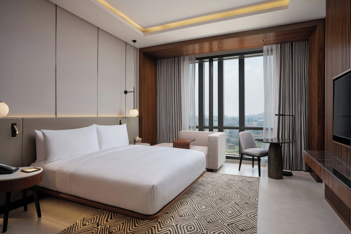 Een moderne hotelkamer met een groot bed, een bureau, een stoel, een televisie en uitzicht op de stad.