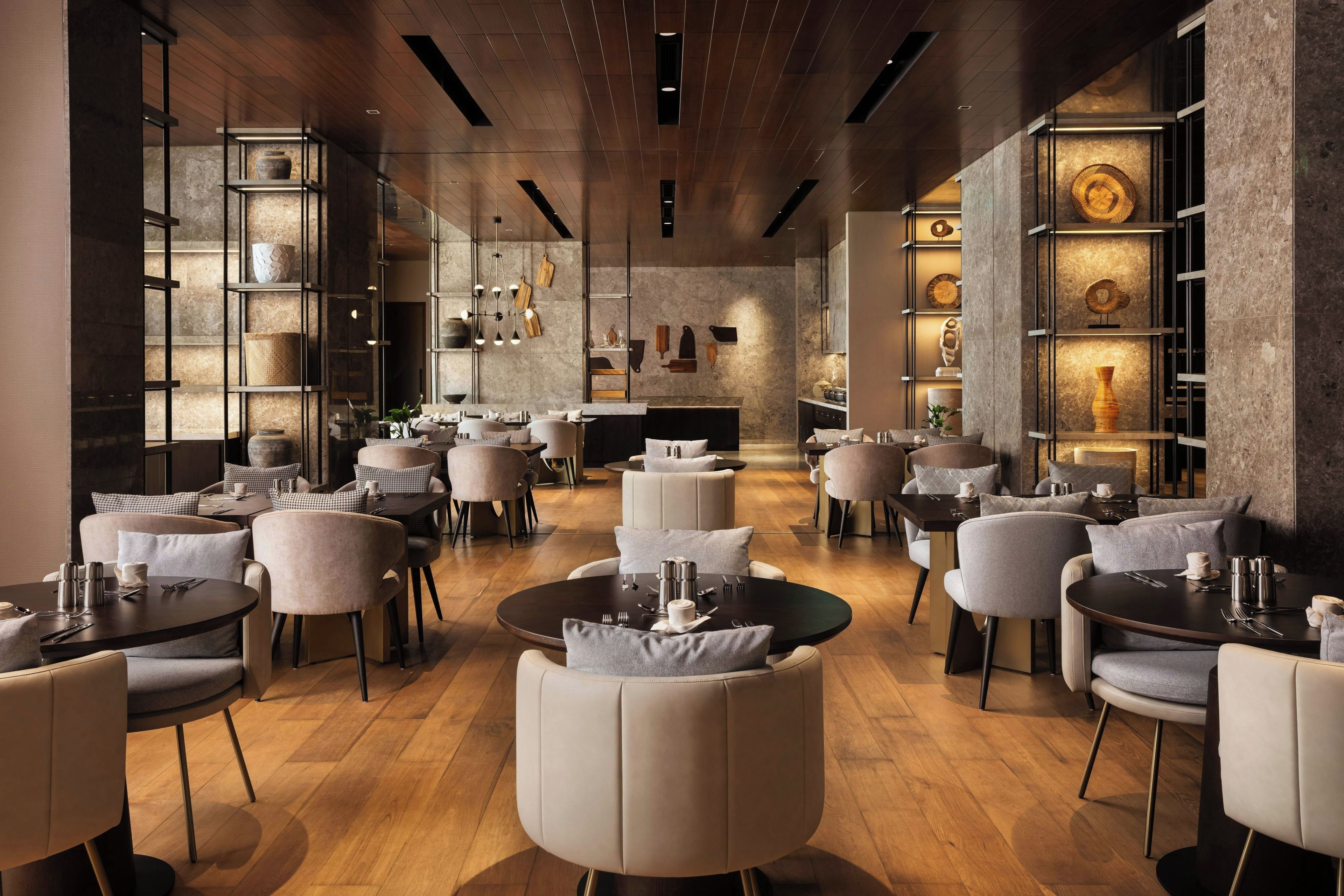 A modern restaurant interior with round tables, cushioned chairs, and a central bar area.