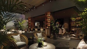 A cozy lounge area with wicker chairs, a round table with a vase and candle, and a brick wall with shelves of bottles. - Kampala Marriott Hotel (Kampala)