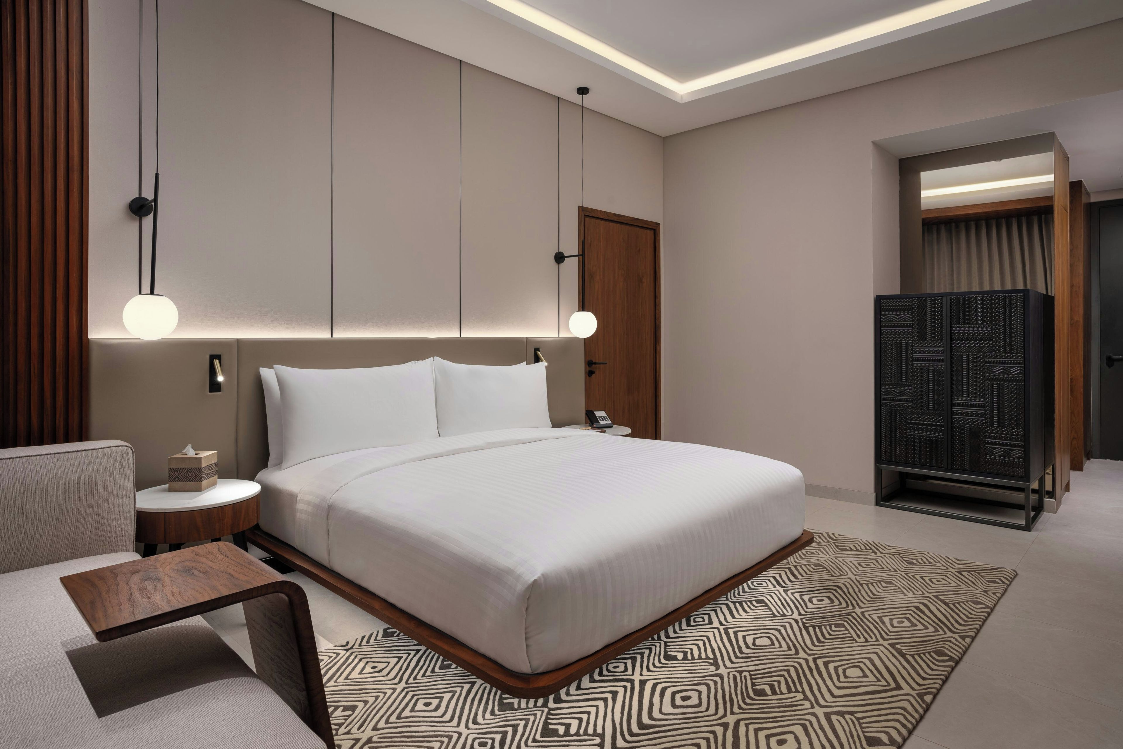 A hotel room with a large bed, bedside tables, a desk, and a wardrobe.