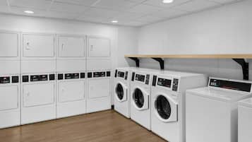 A laundry facility with multiple washing machines and dryers, wooden flooring, and white walls.