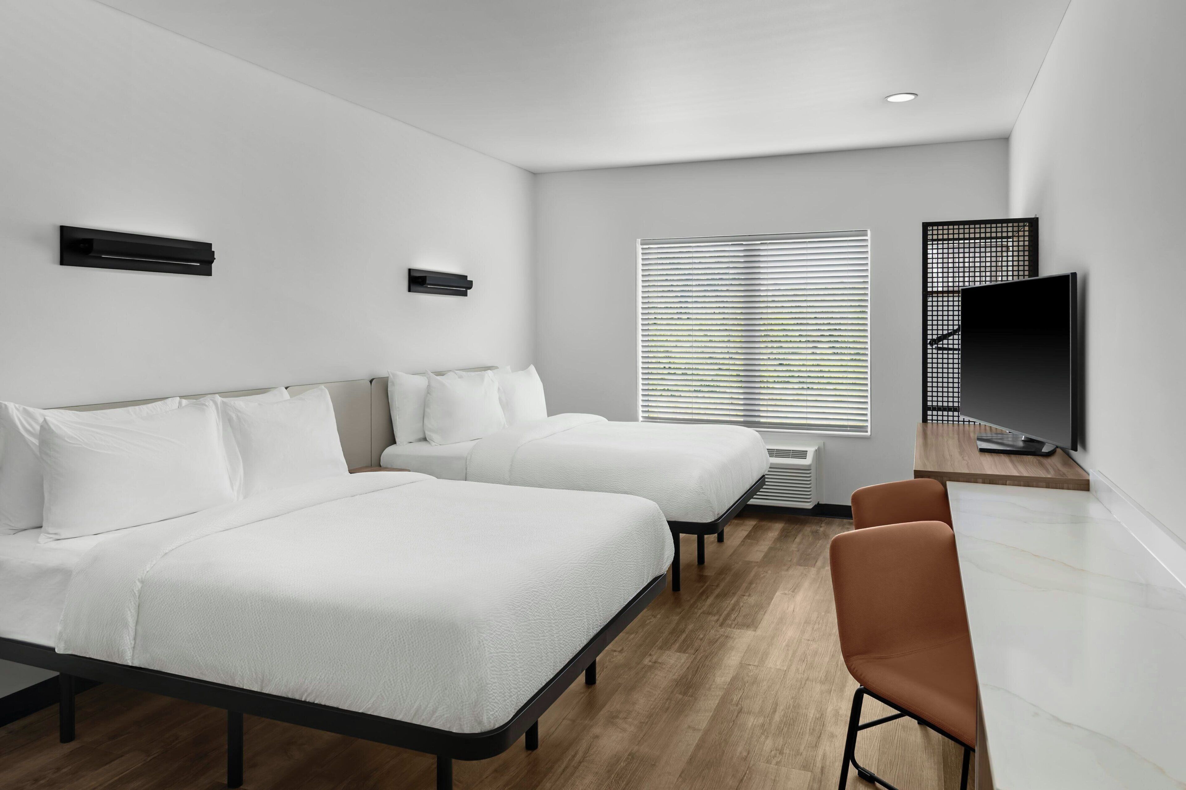 A modern hotel room with two beds, a TV, and a desk.