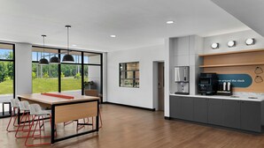 A modern kitchen with a coffee machine, a refrigerator, and a view of a green landscape through large windows. - StudioRes by Marriott Greensboro Airport (Greensboro)