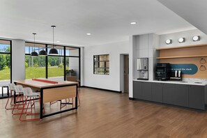 A modern kitchen with a coffee machine, a refrigerator, and a view of a green landscape through large windows. - StudioRes by Marriott Greensboro Airport (Greensboro)