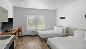 Une chambre d’hôtel équipée d’un bureau, de deux lits, d’une chaise, d’une télévision et d’une fenêtre avec des stores.