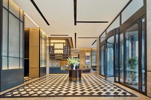 Um lobby moderno com piso xadrez, um balcão de recepção e uma escada que leva aos andares superiores.