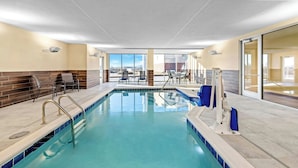 Una piscina interna con acqua cristallina, circondata da poltrone relax e una parete vetrata che offre una vista.