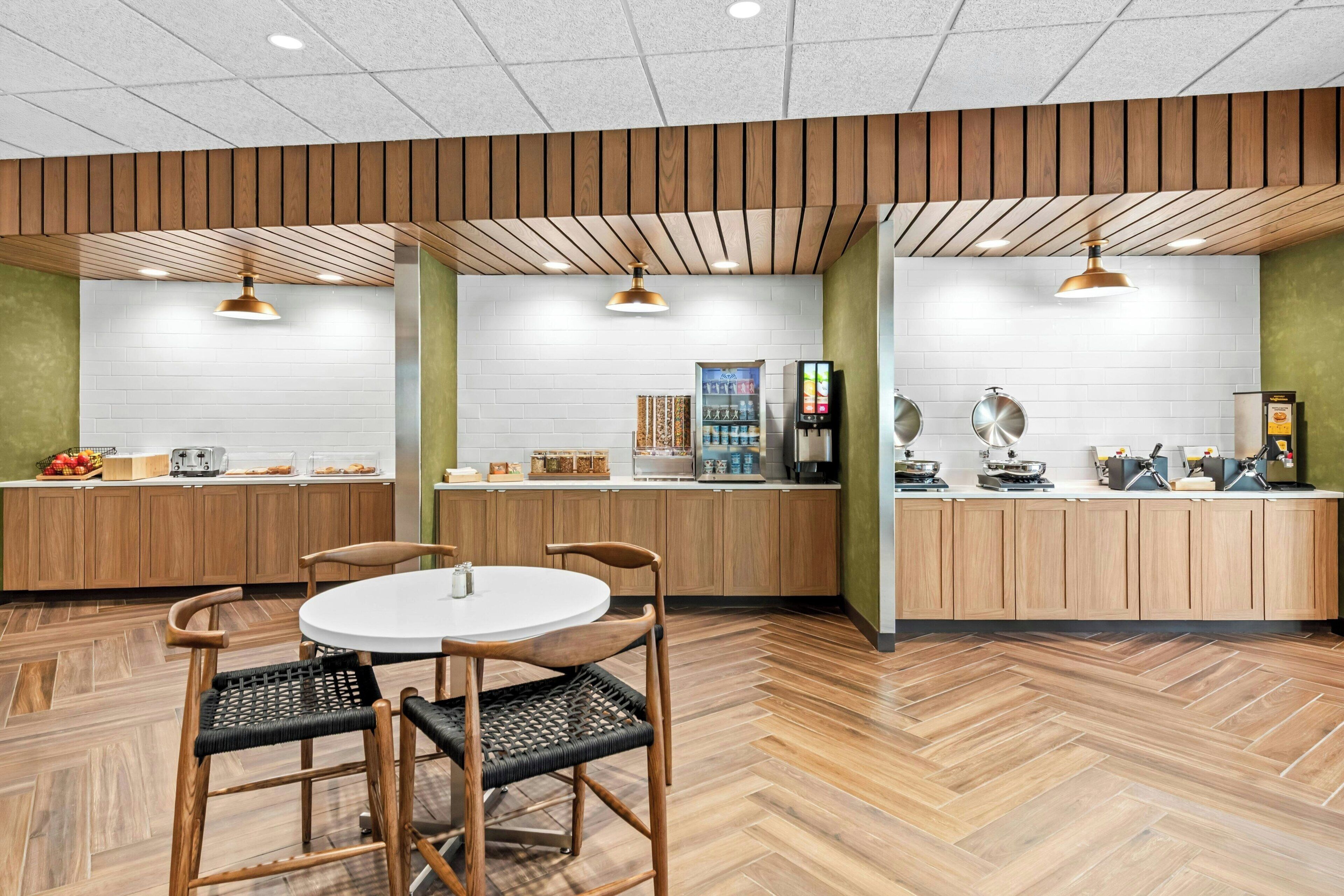 Un espace cuisine moderne avec des meubles en bois, une table de salle à manger ronde entourée de chaises et un plancher à motifs en chevrons.