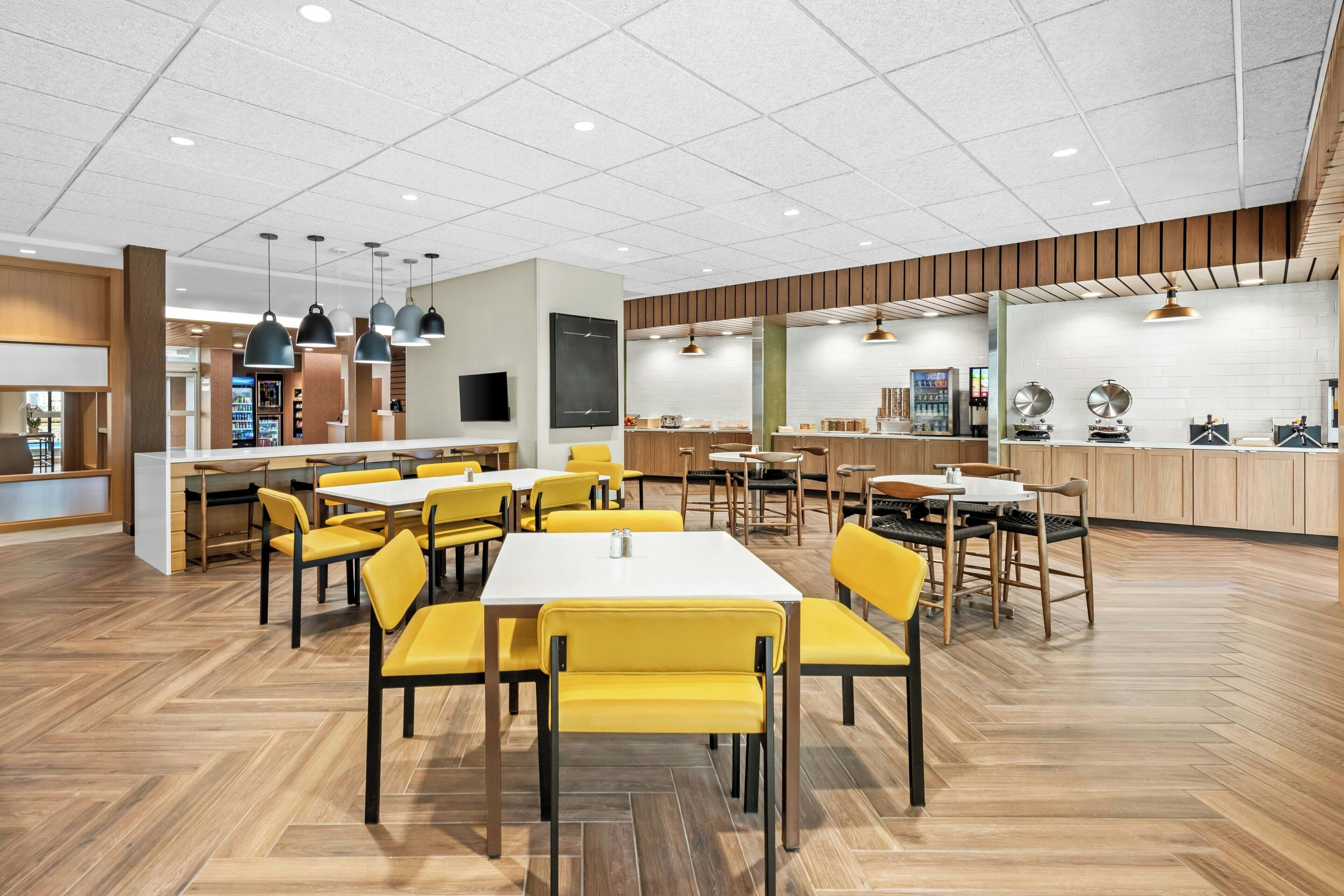 Un comedor moderno con sillas amarillas, mesas de madera e iluminación colgante.