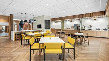 A modern dining area with yellow chairs, wooden tables, and pendant lighting.