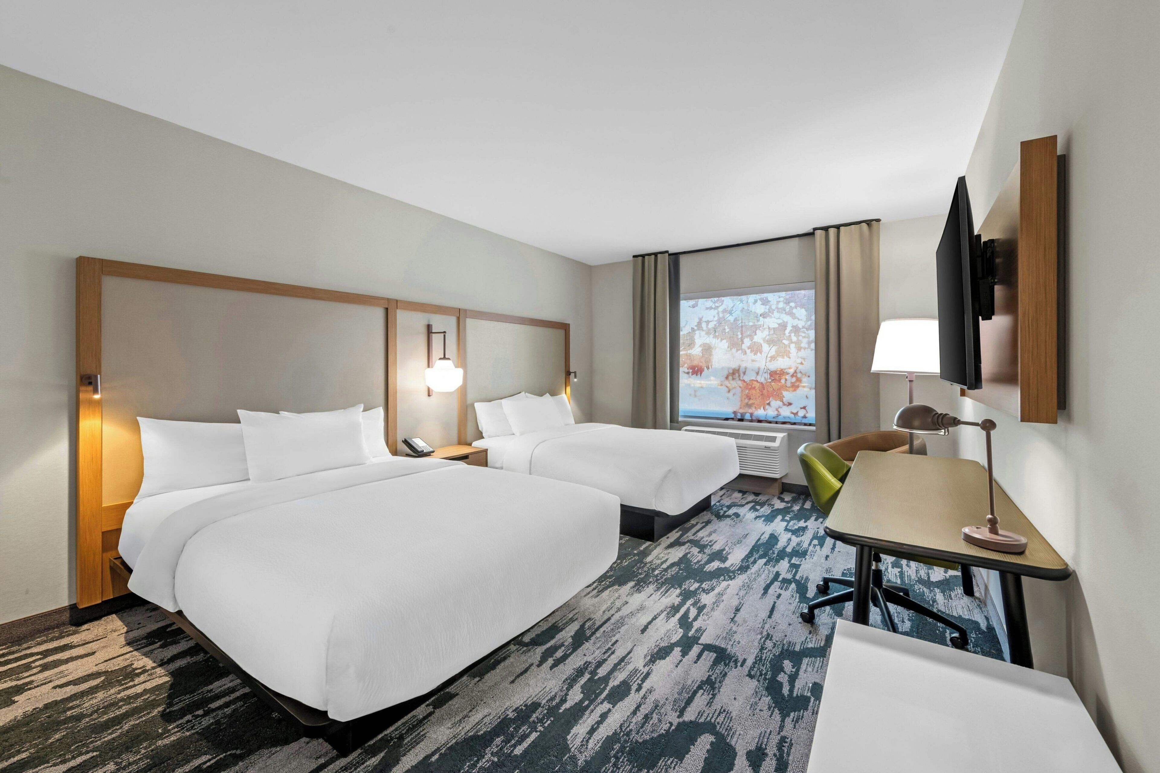 Une chambre d’hôtel avec deux lits, un bureau, une chaise, une télévision et une fenêtre donnant sur un beau paysage.
