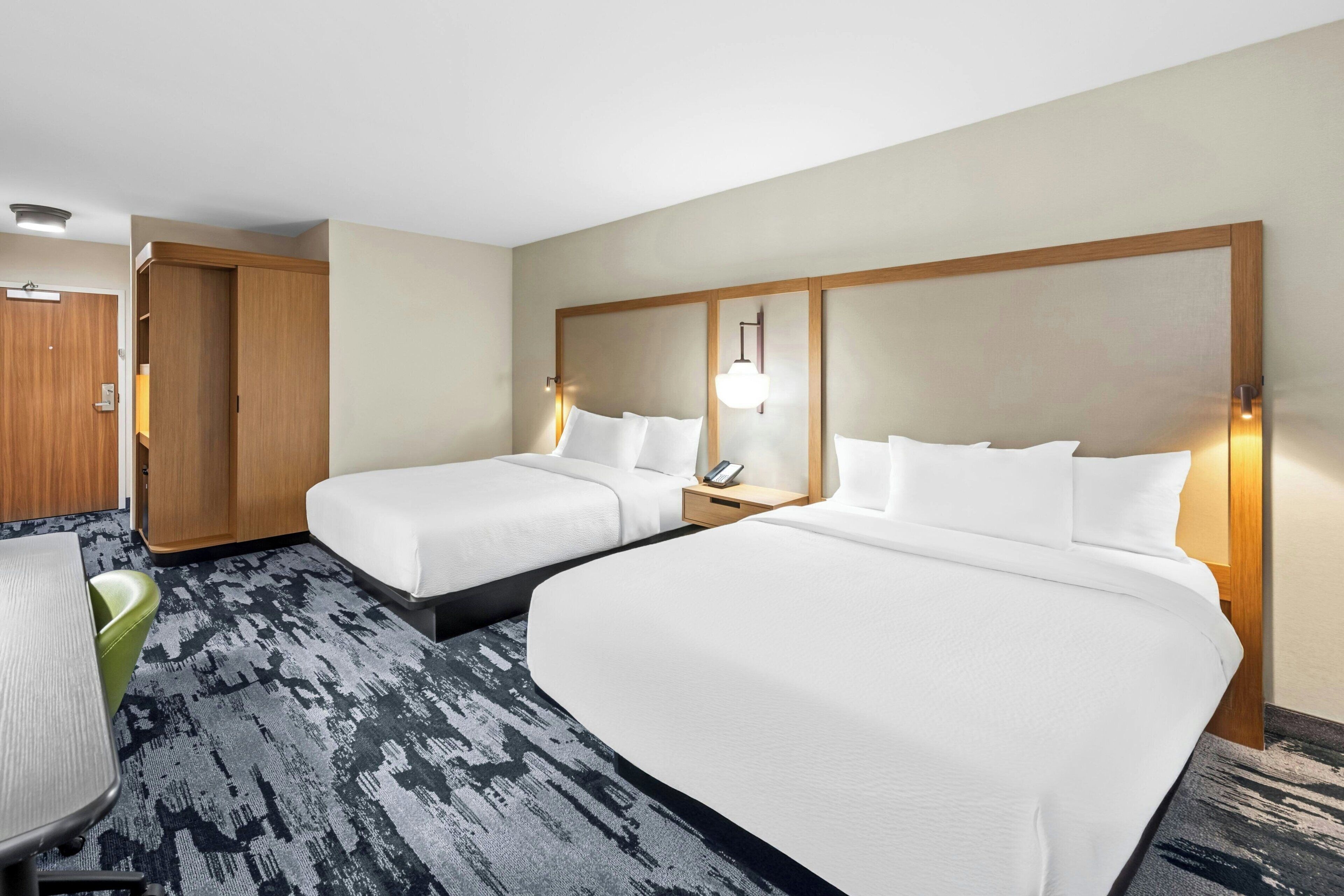 A hotel room with two beds, a desk, a chair, and a carpeted floor.