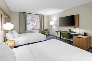 Habitación de hotel con dos camas, un escritorio, una silla, un televisor y una ventana con vistas a un jardín floral.