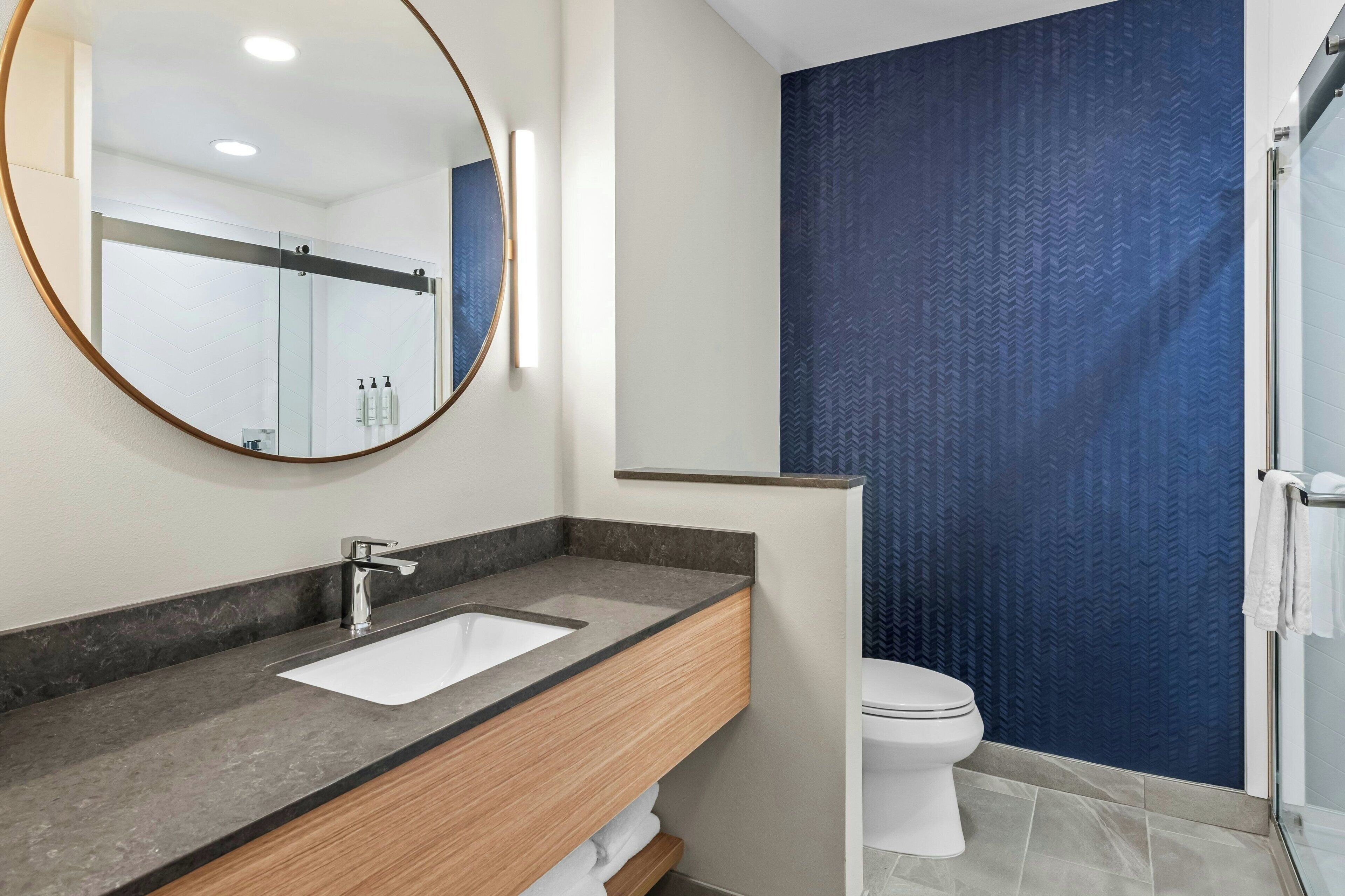 A modern bathroom with a round mirror, a sink, a toilet, and a shower area.