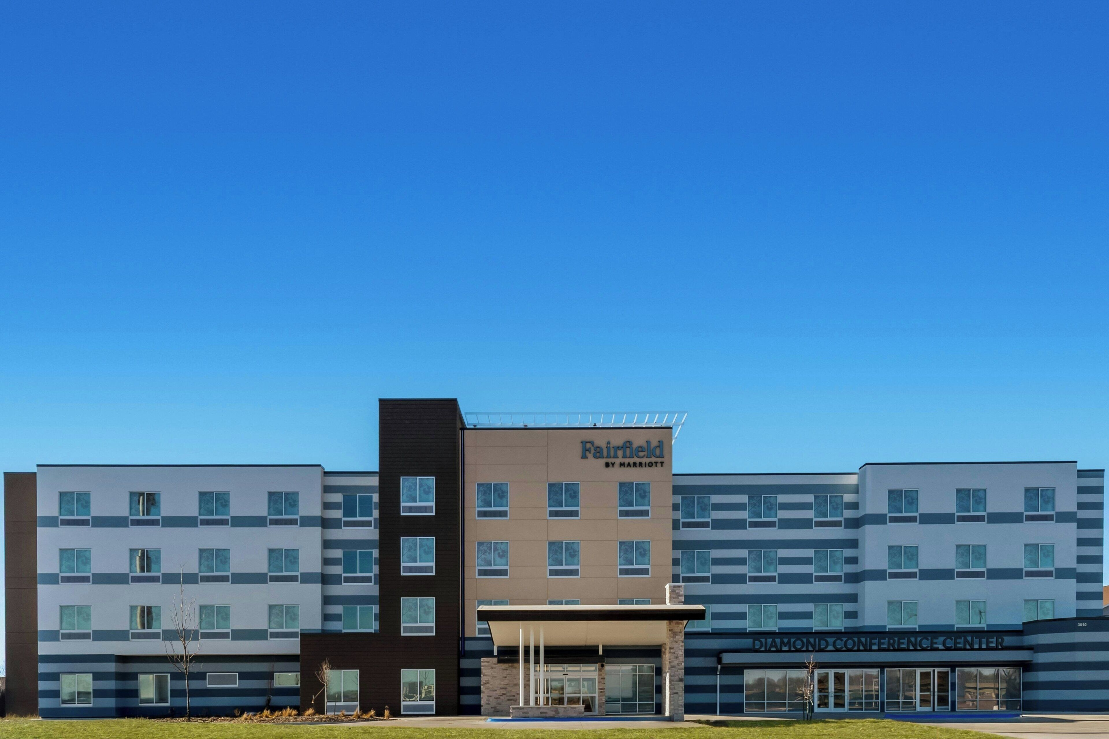 Un hotel Fairfield by Marriott con diseño moderno, que destaca por su entrada principal y un cielo despejado.