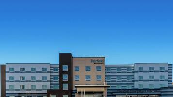 Un hotel Fairfield by Marriott con diseño moderno, que destaca por su entrada principal y un cielo despejado.