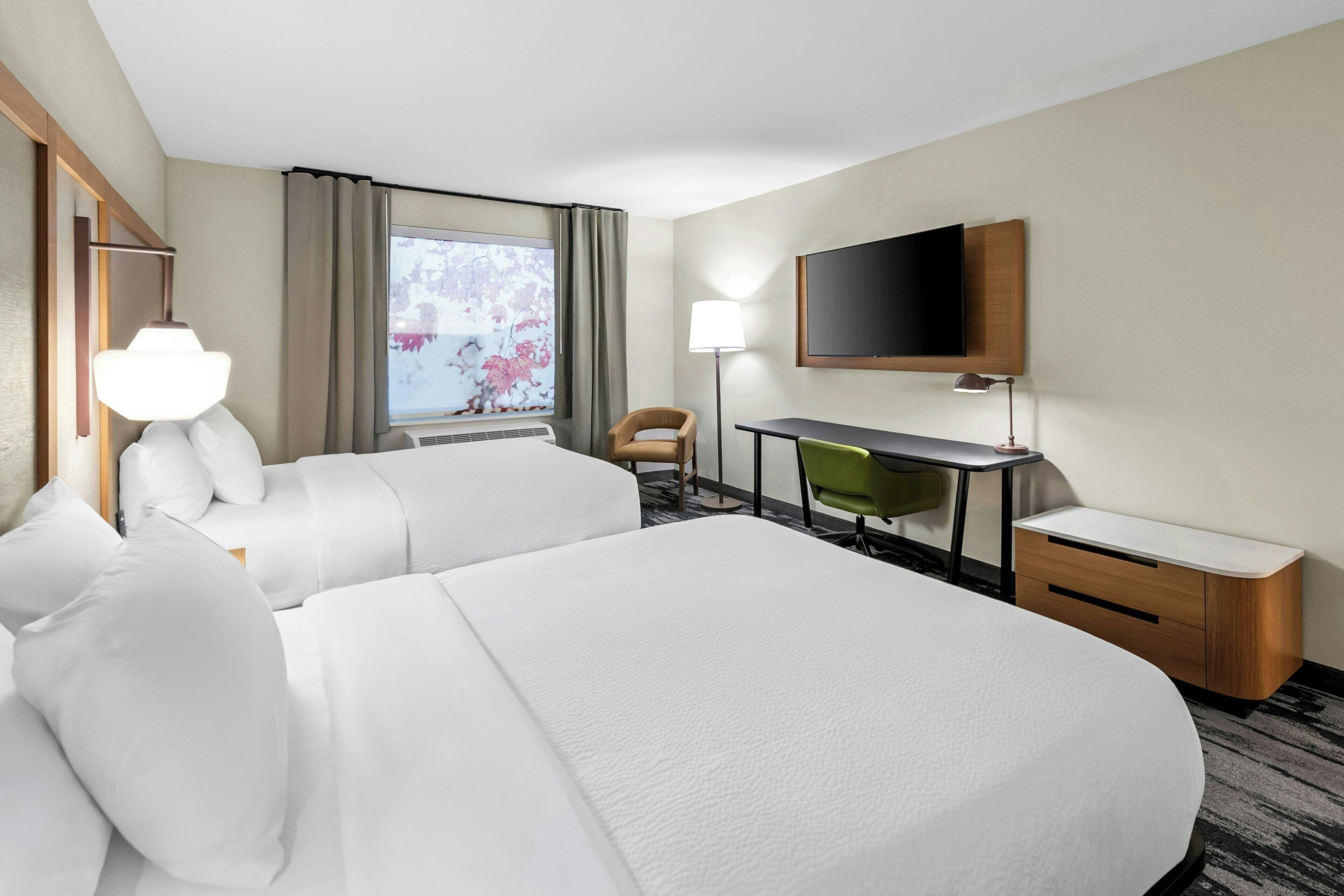 Une chambre d’hôtel avec deux lits, un bureau, une chaise, une télévision et une fenêtre avec des rideaux.