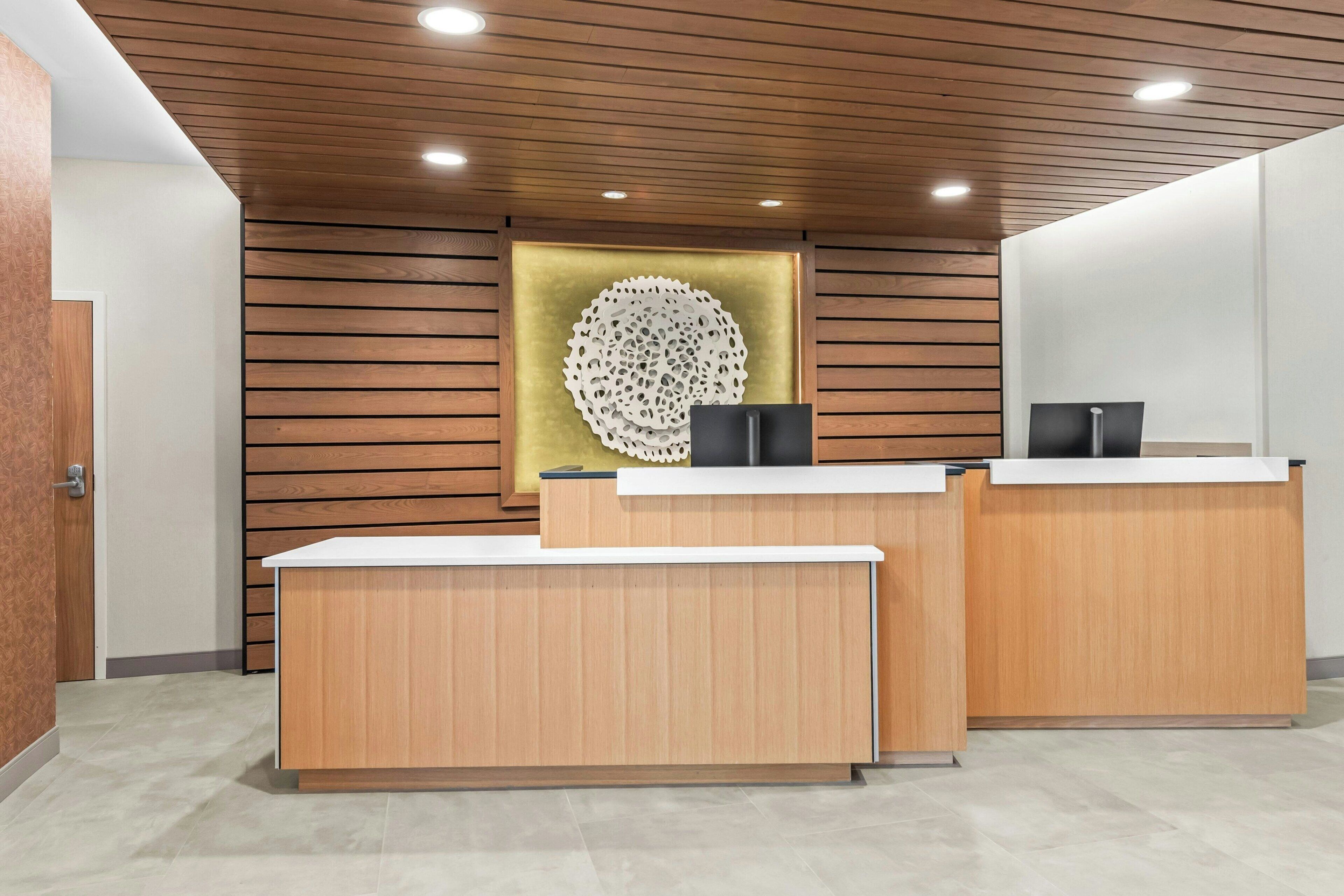 A reception desk with a wooden finish, a decorative wall piece, and a modern ceiling design.