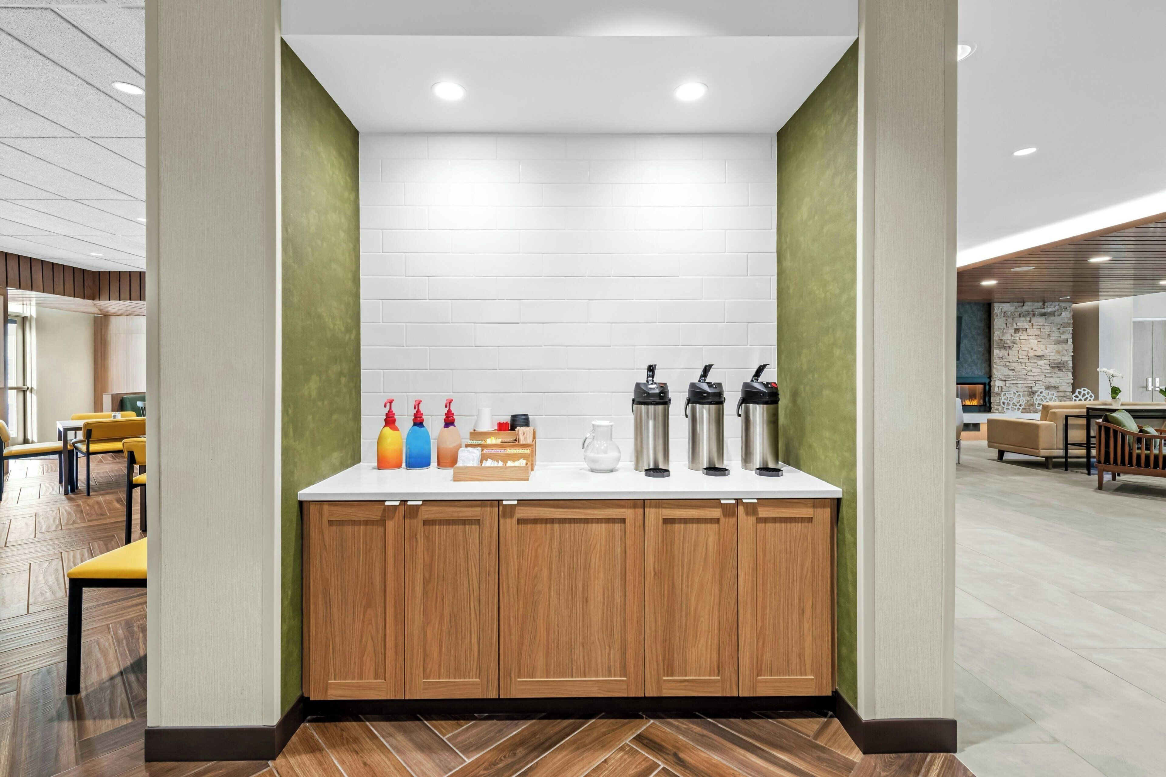 A modern kitchen area with a white countertop, wooden cabinets, and a green accent wall.
