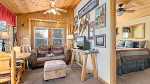 Ein gemütliches Blockhauss-Interieur mit Holzwänden und -decke, einem Sofa, einem Schreibtisch mit Computer und einem Bett mit Decke.