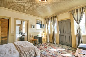 A hotel room with a bed, a desk, a chair, a television, and a door.