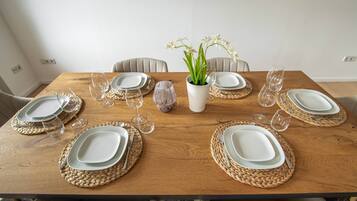 Ein Esstisch, gedeckt mit Tellern, Besteck und Weingläsern, umgeben von gewebten Tischsets und einer Vase mit Blumen.