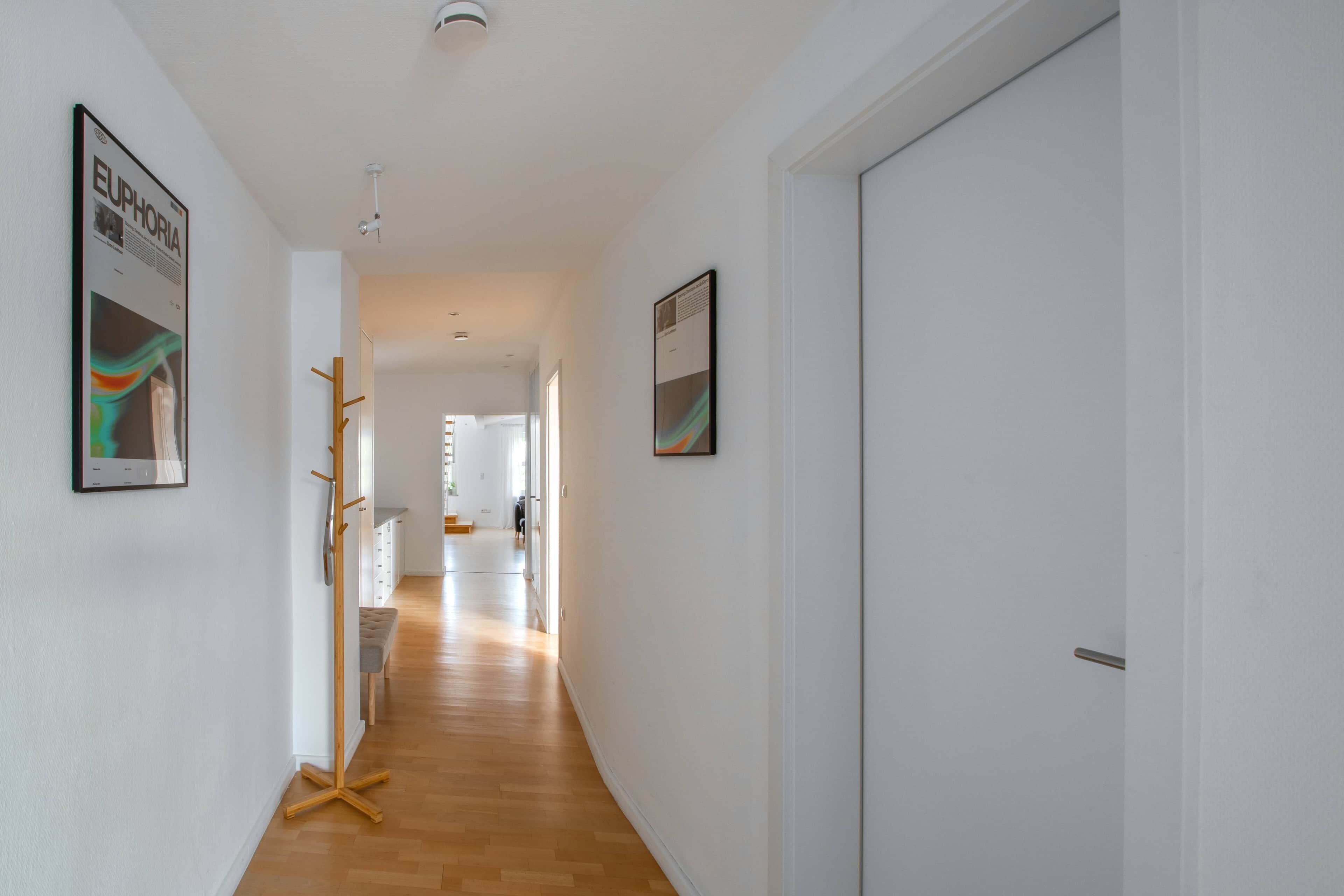 A hallway with wooden flooring, white walls, and framed artwork.