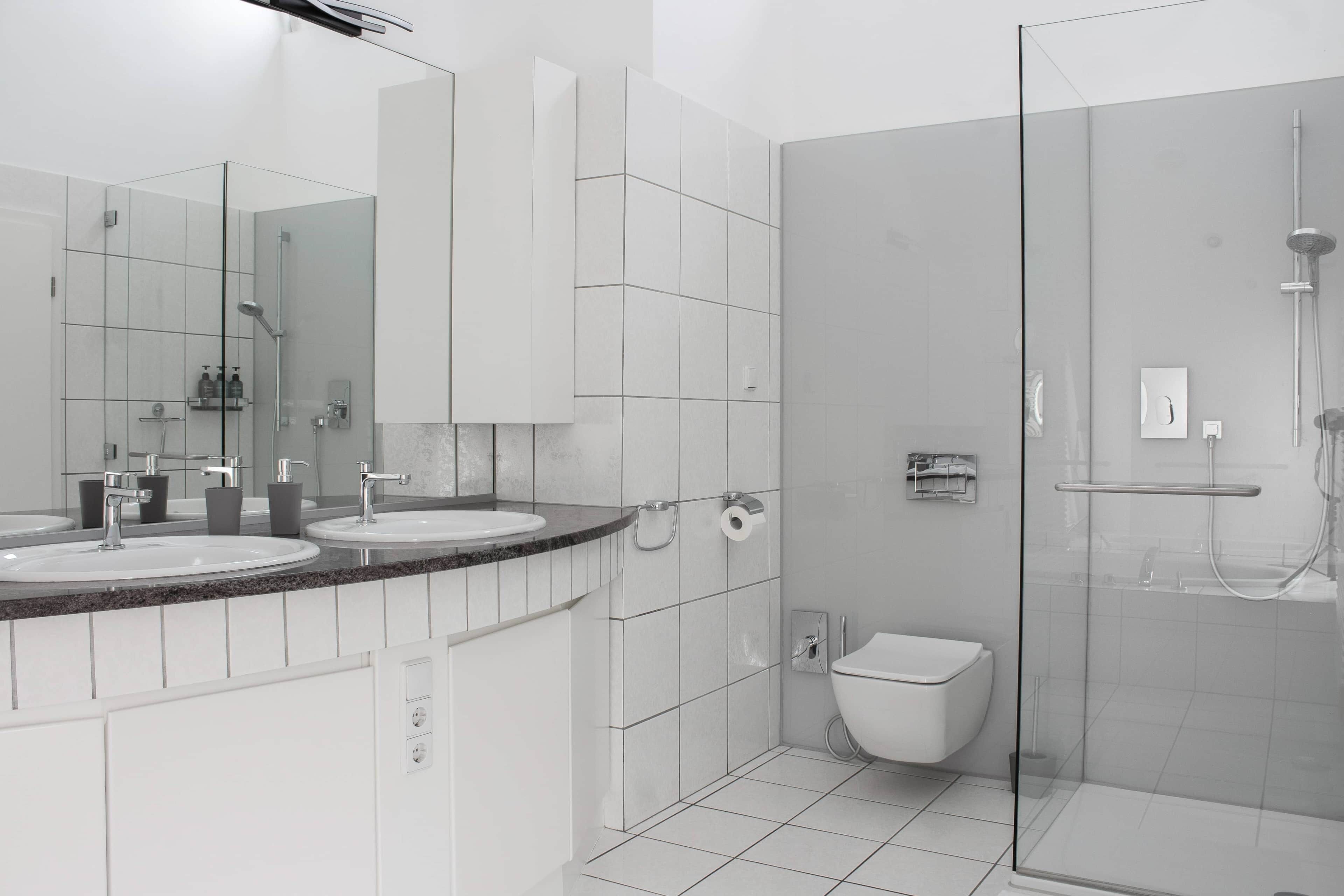Moderni kylpyhuone, jossa on kaksi pesuallasta, lasinen suihkuseinä ja wc.