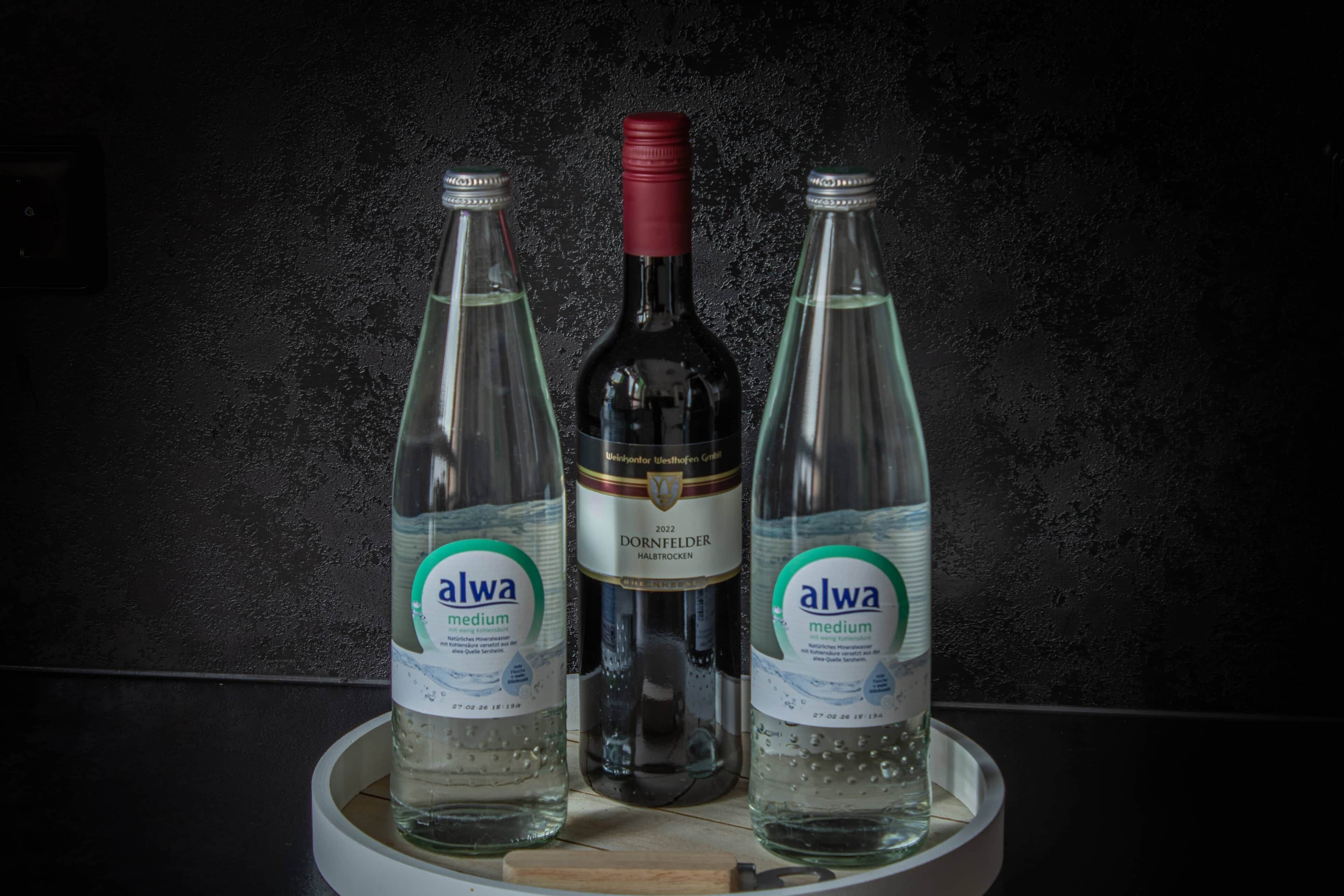 Three bottles of Alwa medium water on a white tray against a dark textured wall.