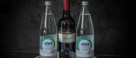 Three bottles of Alwa medium water on a white tray against a dark textured wall.