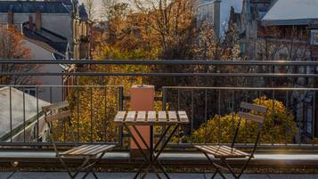A balcony with a table and two chairs, overlooking a cityscape with autumn trees and buildings.