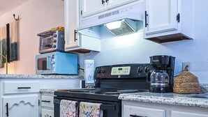 Une cuisine avec des meubles blancs, une cuisinière noire, une machine à café et un grille-pain.